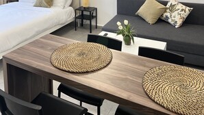 Une chambre d’hôtel moderne comprenant un lit, un canapé, une table à manger avec des sets de table en fibres tressées et deux œuvres d’art accrochées au mur.