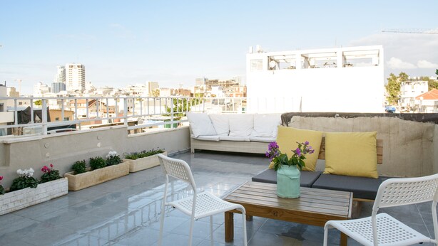 Une terrasse sur le toit avec un canapé blanc, deux chaises blanches, une table en bois et des plantes en pot.