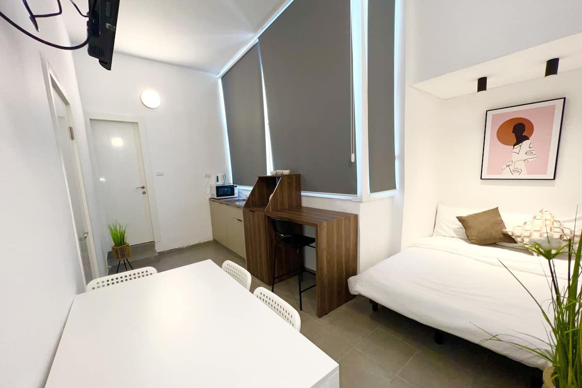 A compact room with a bed, a desk, and a small kitchenette.