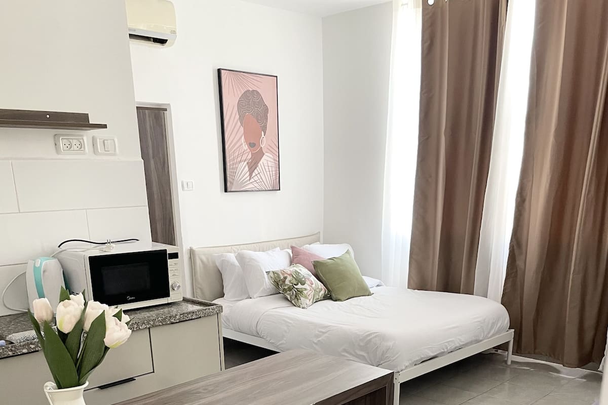 A modern bedroom with a bed, bedside table, and a small desk area with a microwave.