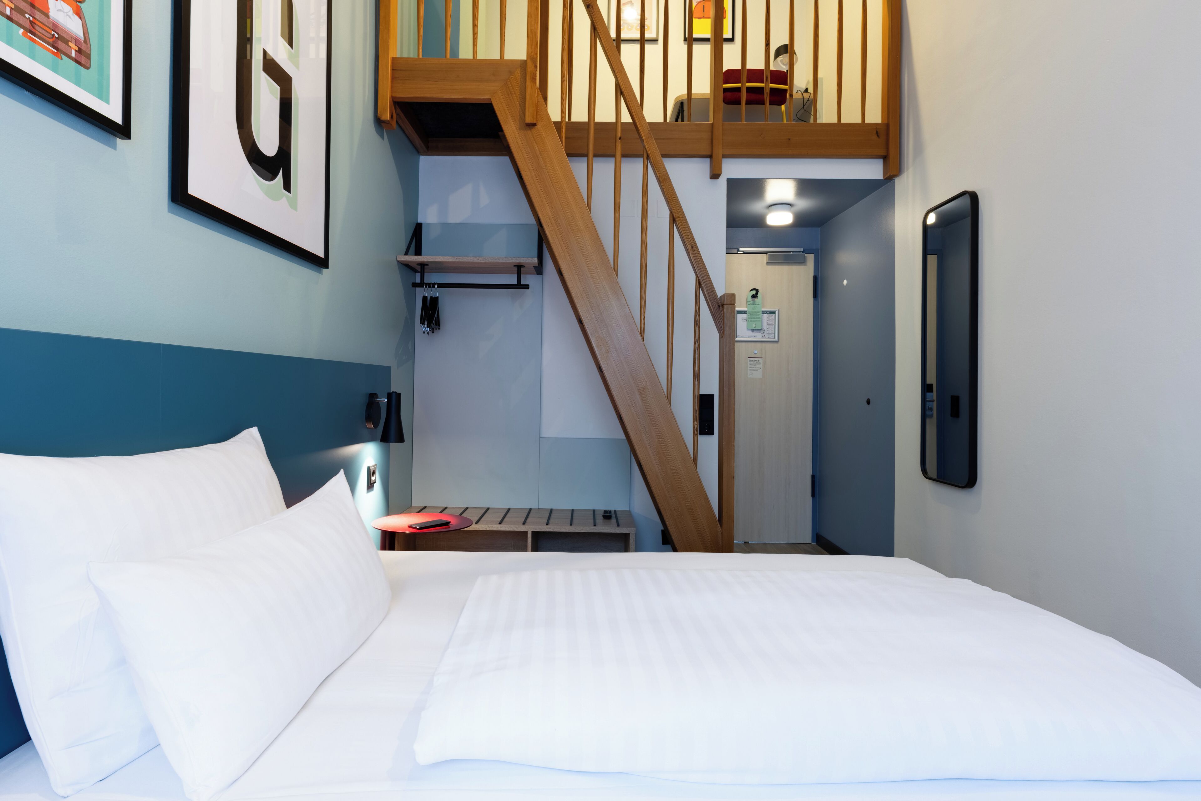 A bedroom with a bed, a wooden staircase, a desk, and a wall-mounted phone.
