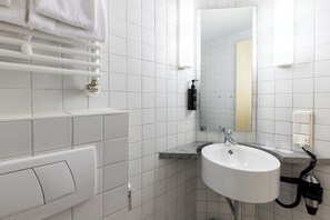 Une salle de bain moderne avec des carreaux blancs, un lavabo blanc, un miroir et un porte-serviettes.