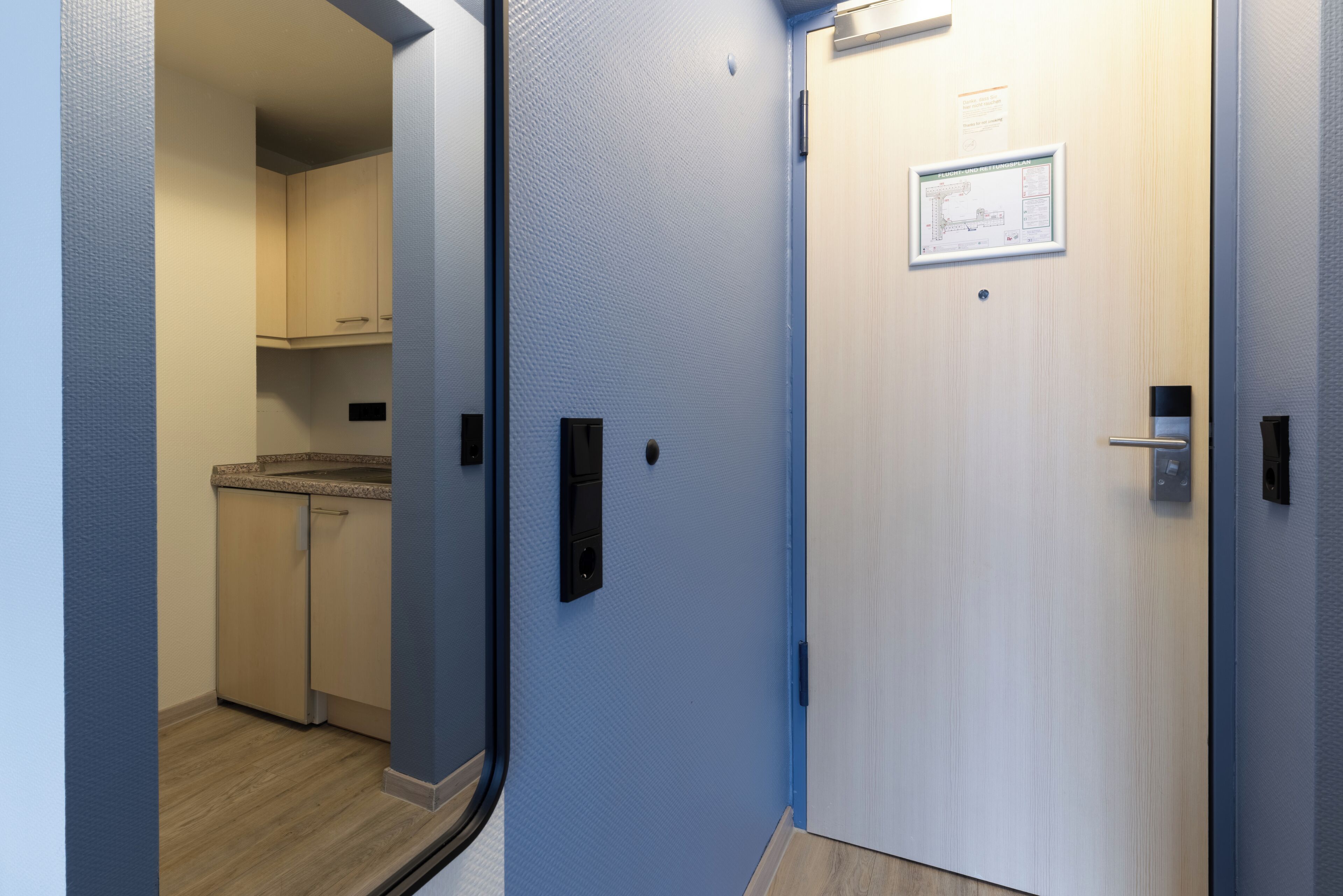 Un pasillo con una zona de cocina, una puerta con un mapa y un interruptor de luz.