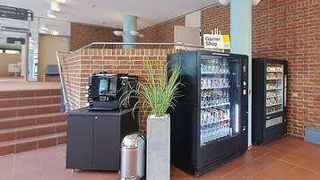 Un área de recepción con pared de ladrillo, un letrero de Garner Shop, máquinas expendedoras y un cubo de basura.