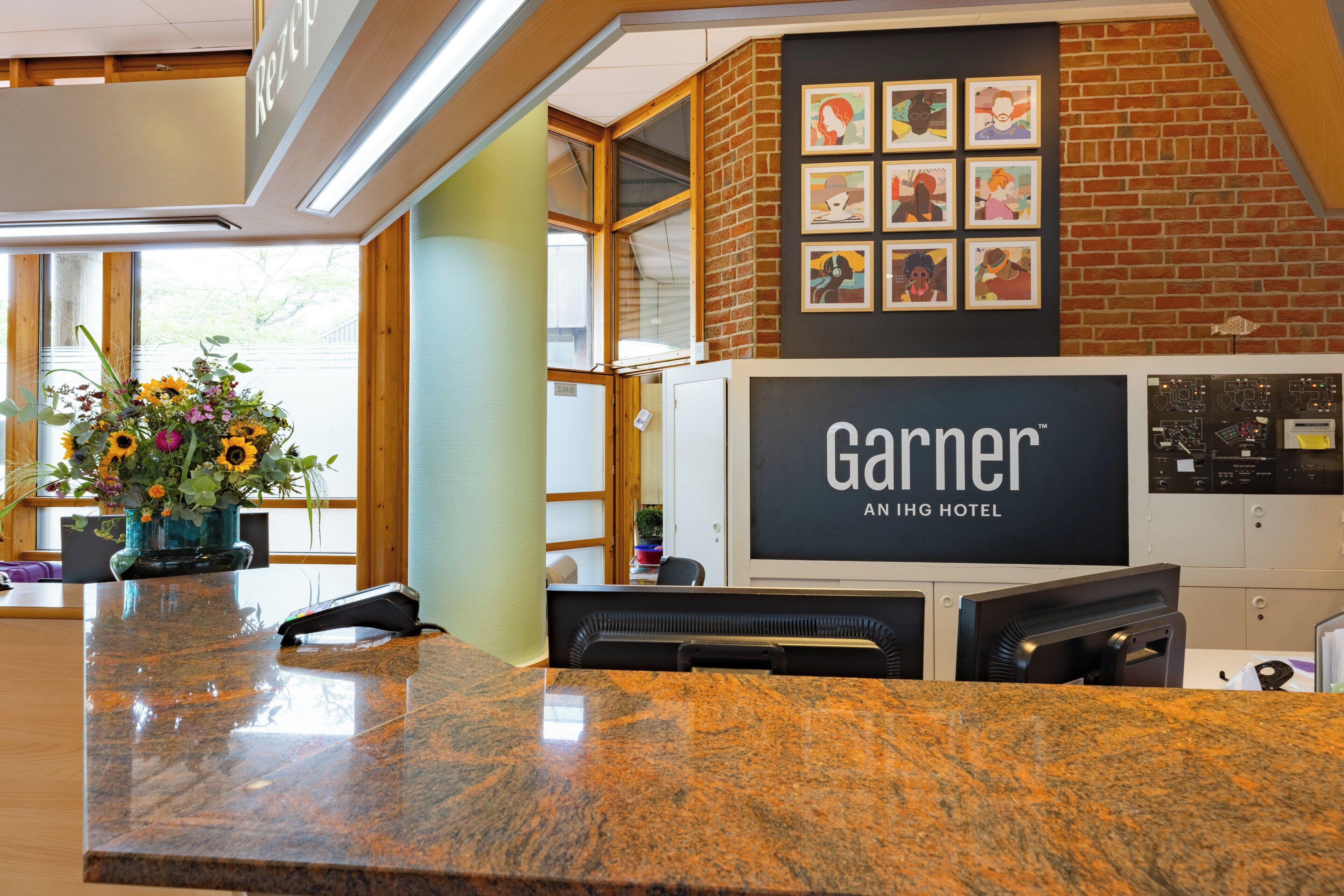 Un comptoir d’accueil d’hôtel avec un revêtement en granit, un vase de fleurs et une enseigne indiquant « GARNIER ANING HOTEL ».