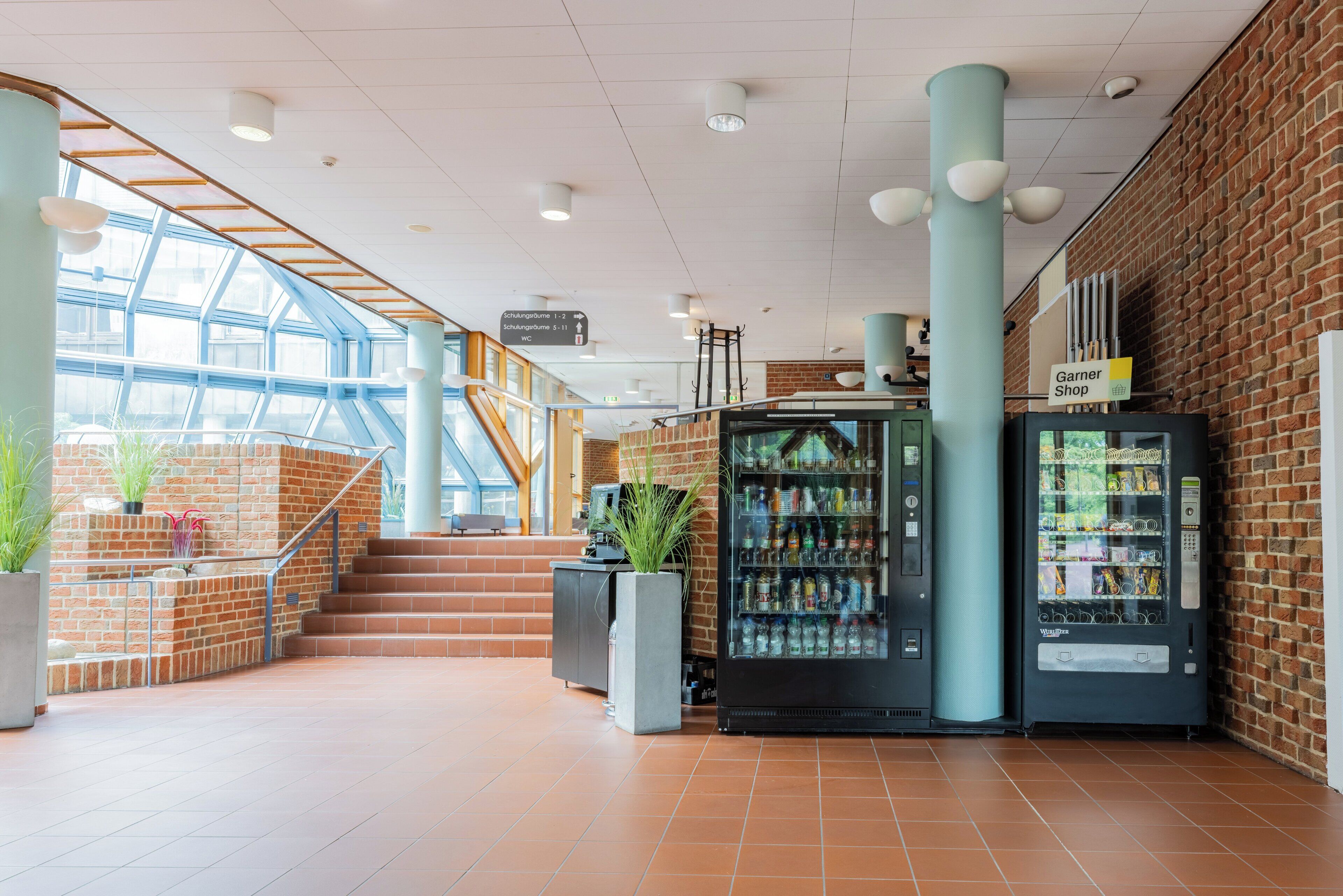 Een ruime lobby met een trap, automaten en een Garner Shop.