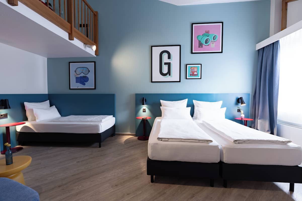 Een hotelkamer met twee bedden, een houten plafond en een blauwe muur met ingelijste foto's.