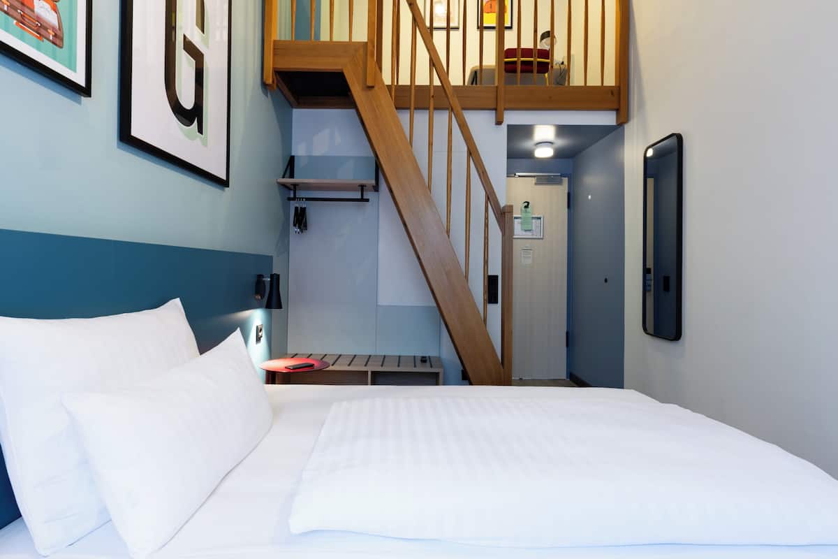 Een hotelkamer met een bed, een houten trap, een klein tafeltje en een aan de muur bevestigd telefoontoestel.