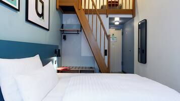 A hotel room with a bed, a wooden staircase, a small table, and a wall-mounted phone.