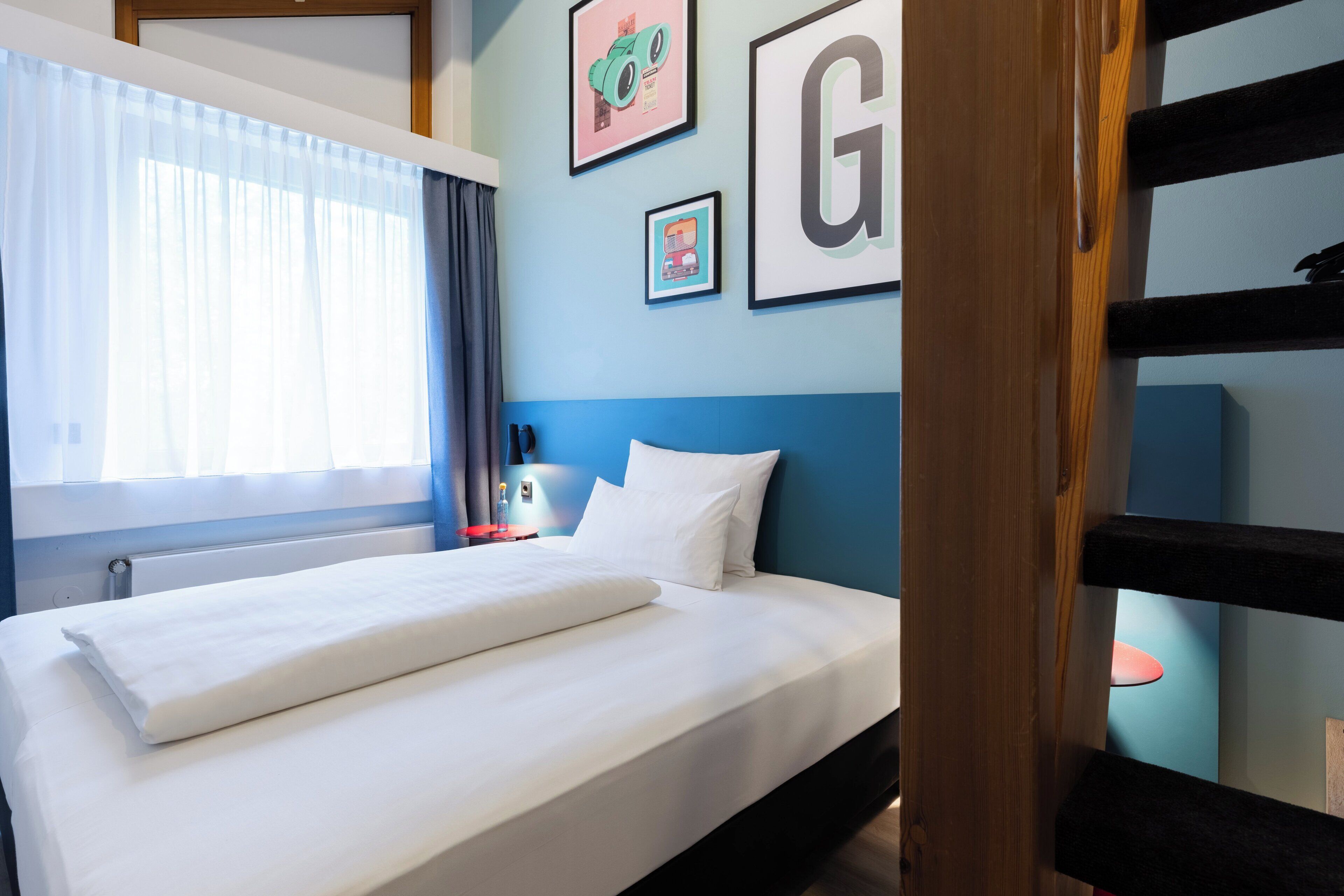 Een net opgemaakt bed met witte lakens, een blauw hoofdbord en een muur met ingelijste foto's.