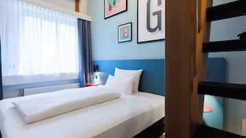Een net opgemaakt bed met witte lakens, een blauw hoofdbord en een muur met ingelijste foto's.
