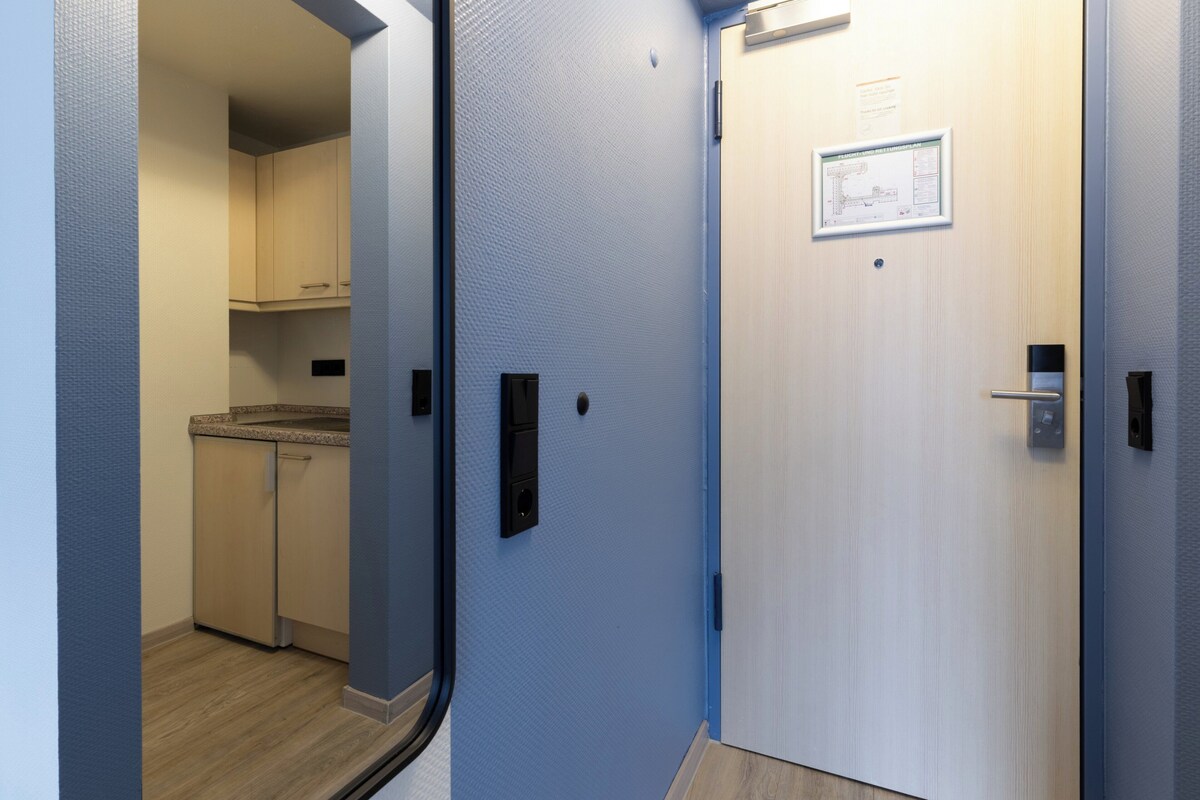 Un couloir avec un coin cuisine, une porte ornée d’une carte et un interrupteur.
