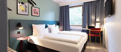 A hotel room with a bed, a desk, a chair, and a TV on the wall.