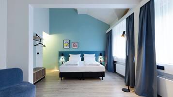 Habitación de hotel moderna con cama, lámparas de noche, pared azul y vista al exterior.