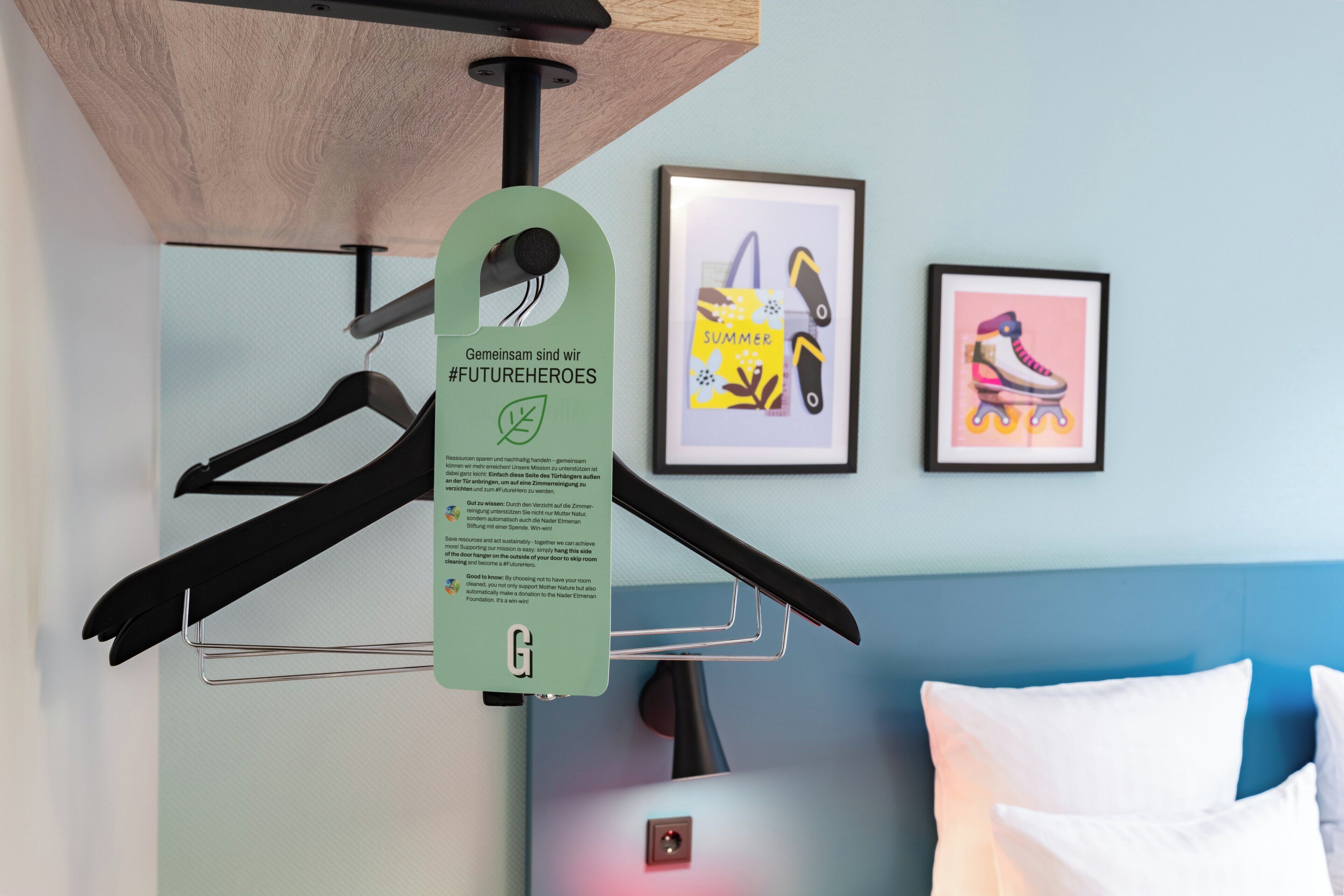 A hotel room with a bed, a hanging coat rack, and two framed pictures on the wall.
