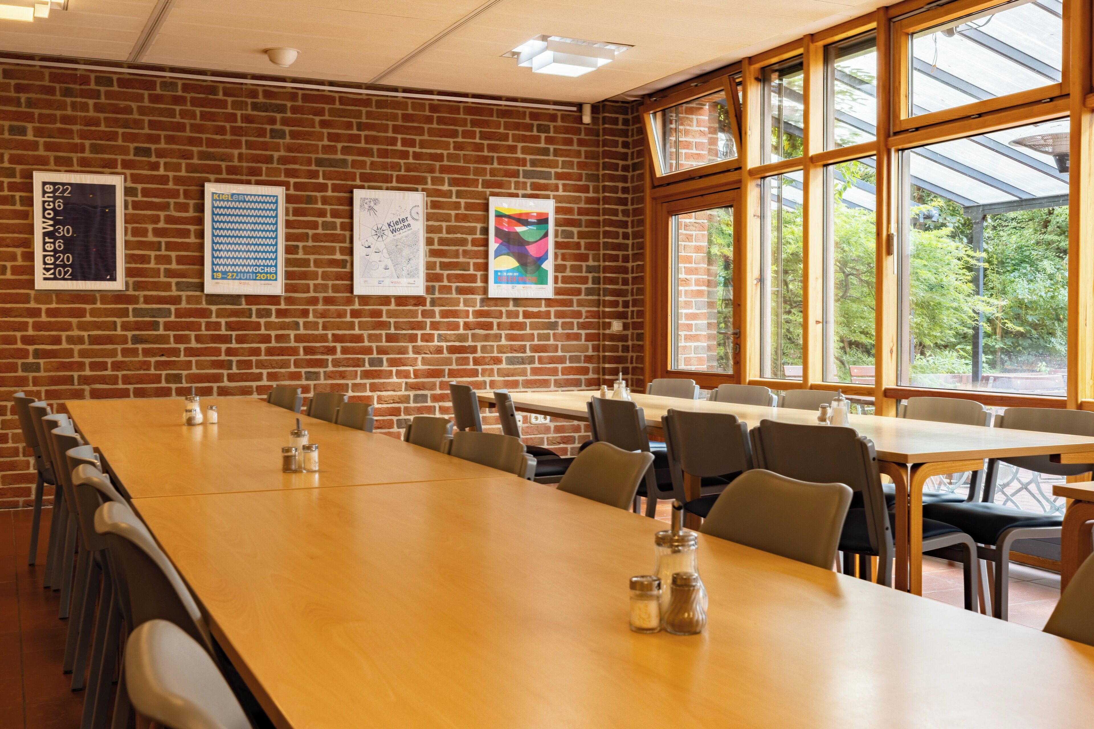 A conference room with a long wooden table, multiple chairs, and large windows offering a view of greenery outside.