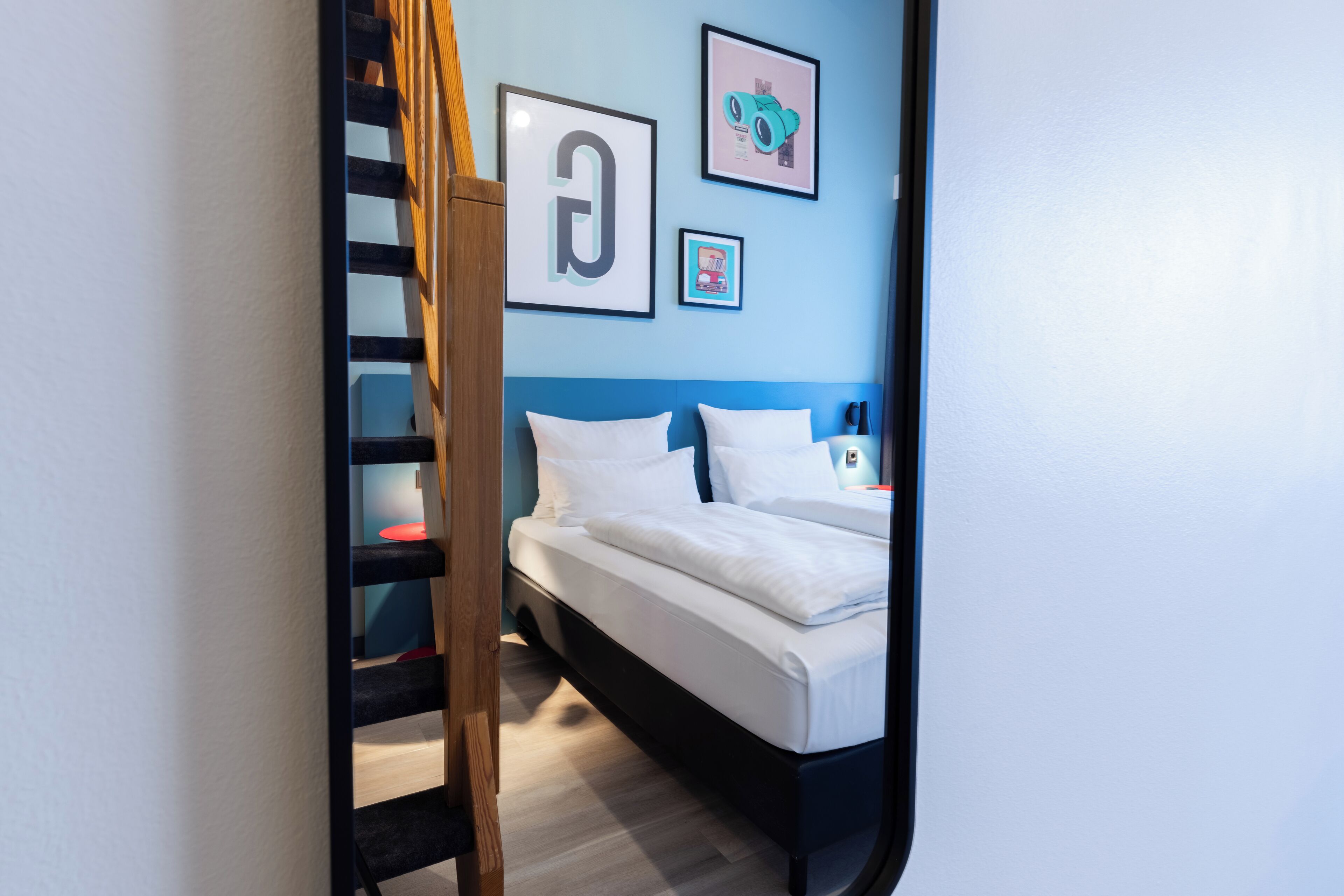 Ein Schlafzimmer mit einem Bett, einer Holzleiter und einer blauen Wand mit gerahmten Bildern.