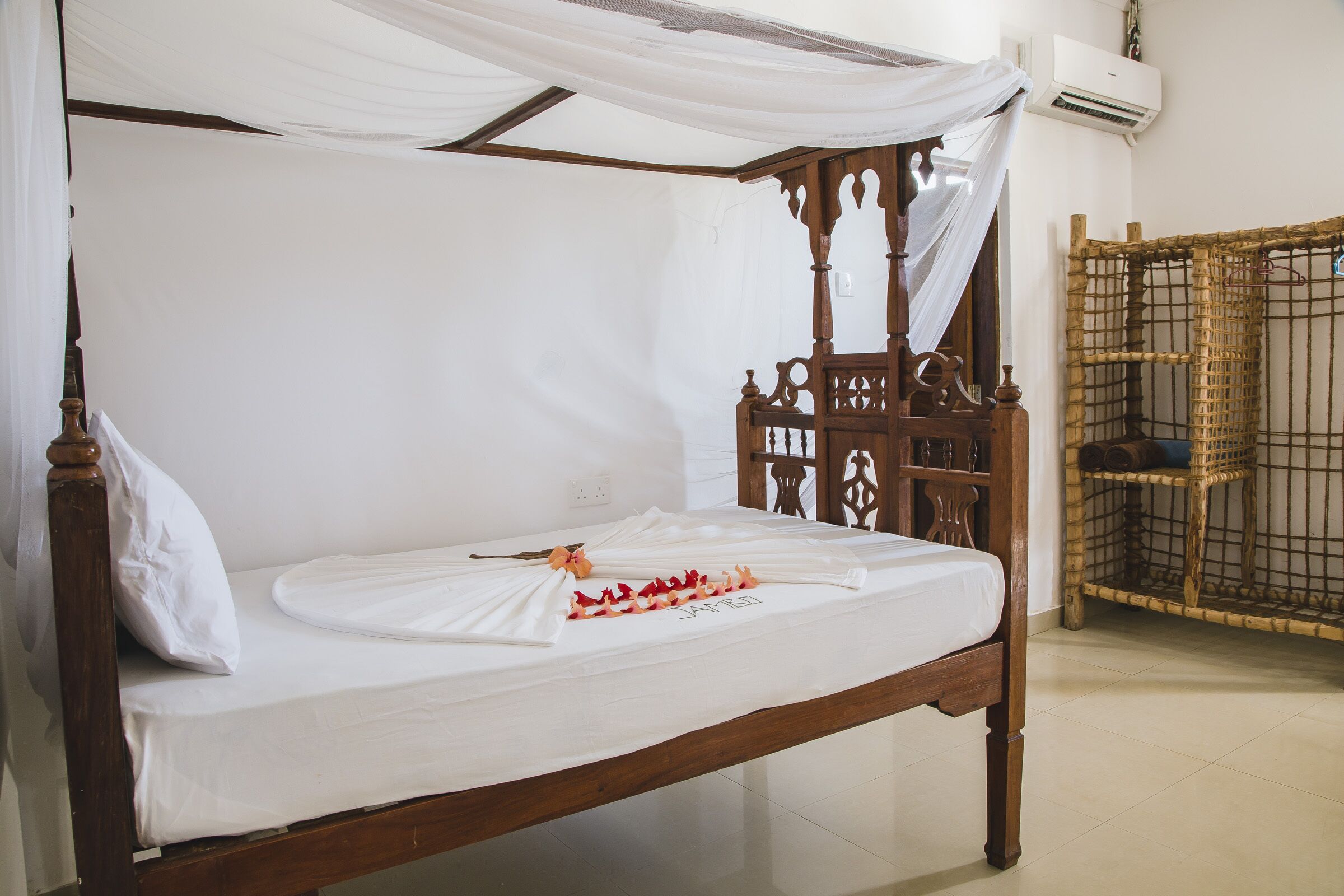 Una cama con dosel de madera con ropa de cama blanca y un arreglo decorativo de flores.