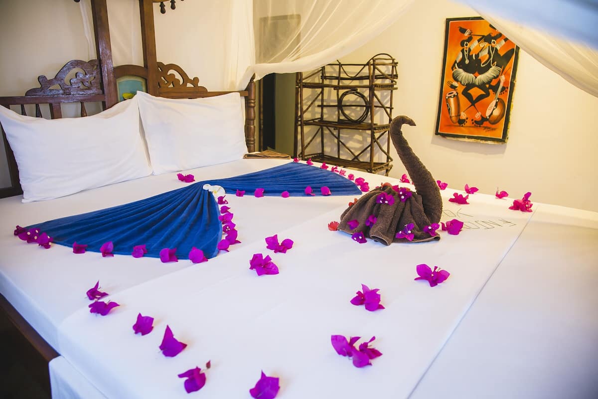 Un lit recouvert d’une couvre-lit bleue et orné d’oreillers blancs, le tout décoré de pétales de fleurs roses.