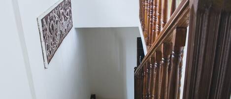 Una escalera con balaustres de madera y barandilla, que lleva a un rellano con una ventana y un panel decorativo.
