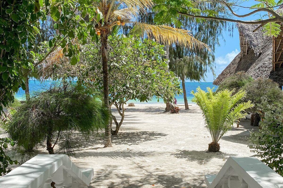 Un sentier menant à une plage bordée de constructions aux toits de chaume et d’une végétation luxuriante.
