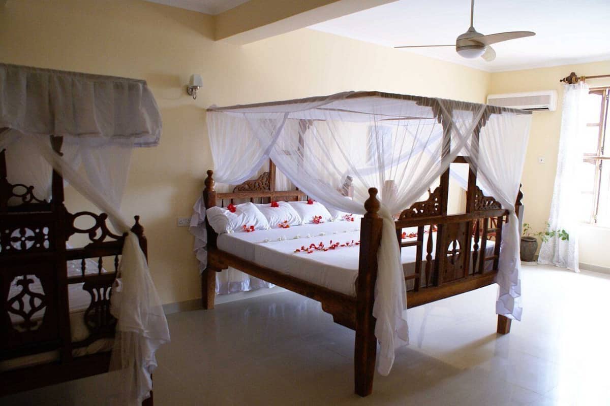 Un lit à baldaquin, une commode en bois et un ventilateur de plafond.