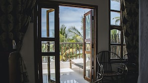 Een open schuifdeur die uitkomt op een balkon met uitzicht op palmbomen en een hangmat.