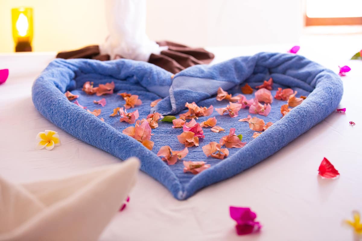 Une serviette disposée en forme de cœur sur un lit, parsemé de pétales de fleurs.