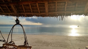 Een strand met een rieten constructie, zand en de oceaan op de achtergrond.
