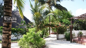 Een restaurantsbord, een palmboom en een tuin met een stenen muur en een pergola.
