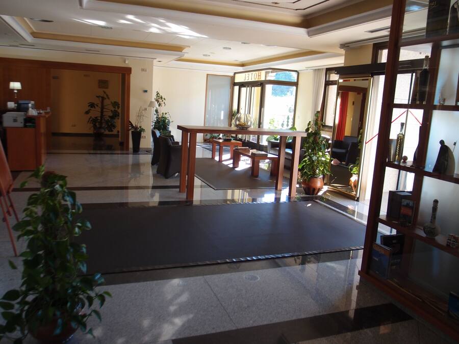 Um hall de hotel com balcão de recepção, área de estar e uma vitrine de vidro com objetos.