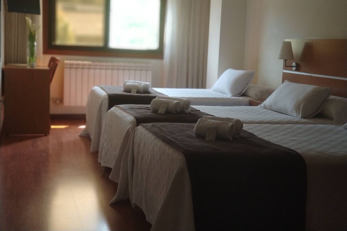 A hotel room with two beds, a desk, and a window with curtains.
