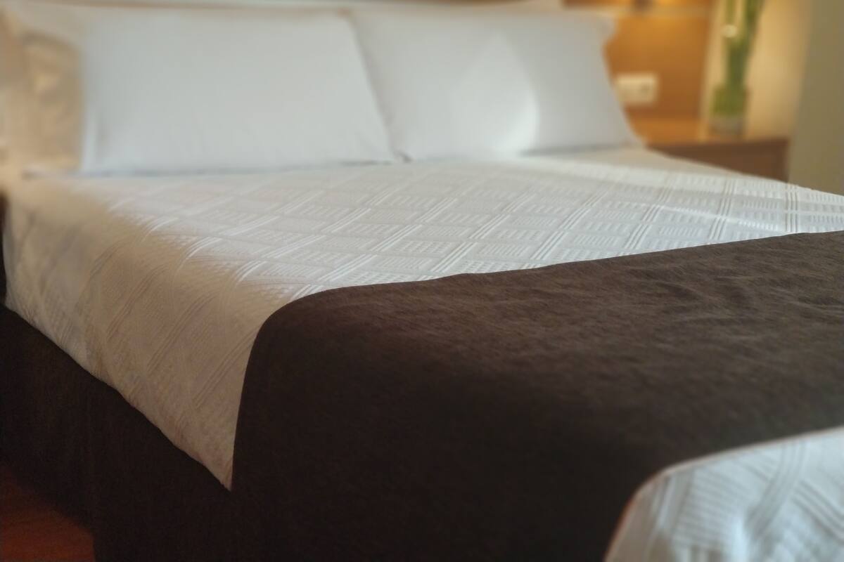 A neatly made bed with white bedding and a dark-colored throw blanket.