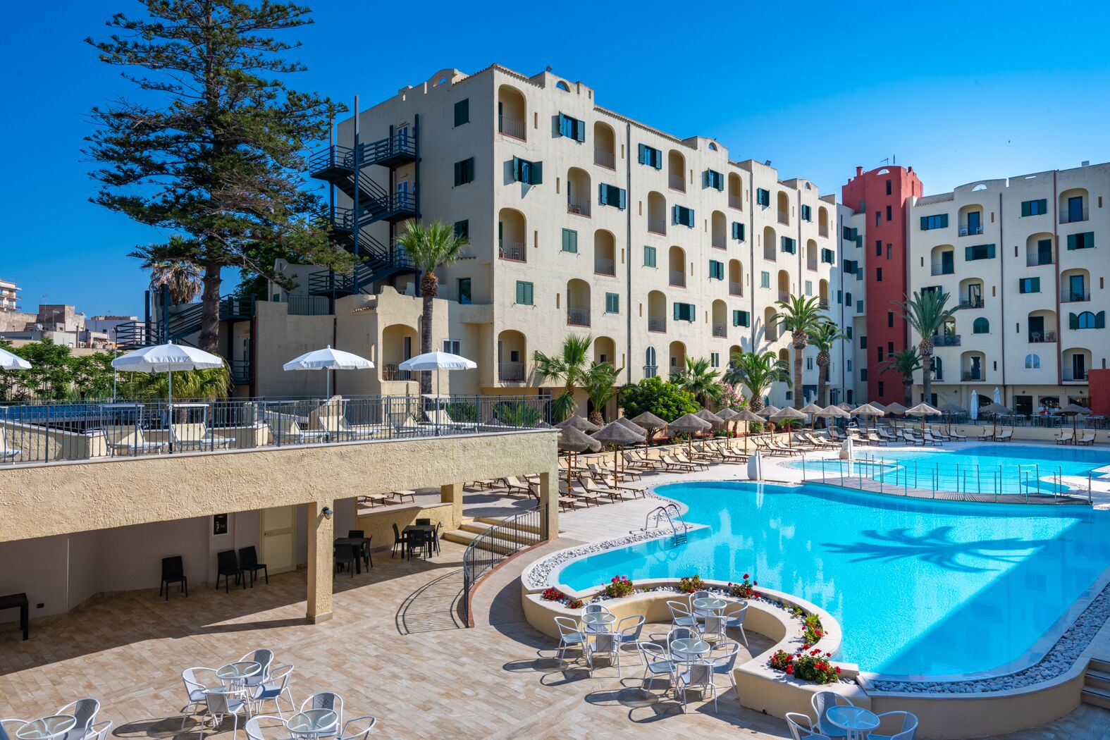 A hotel with a large swimming pool, outdoor seating, and a palm tree.