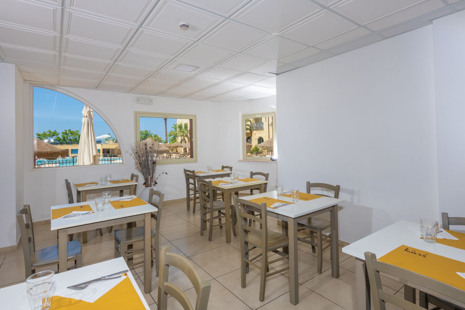 Un espace repas avec des tables et des chaises, de grandes fenêtres offrant une vue dégagée et un plafond doté d’un éclairage encastré.