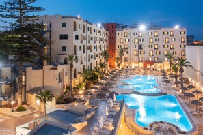 Un hotel con varias piscinas, palmeras y un área exterior bien iluminada.