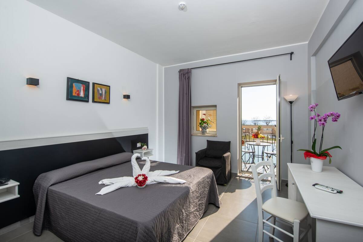 Moderni hotellihuone, jossa on suuri sänky, työpöytä, tuoli ja parveke, jolta on näkymä.
