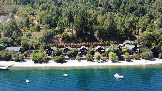 En kystresort med flere hytter, en sandstrand og skov i baggrunden.