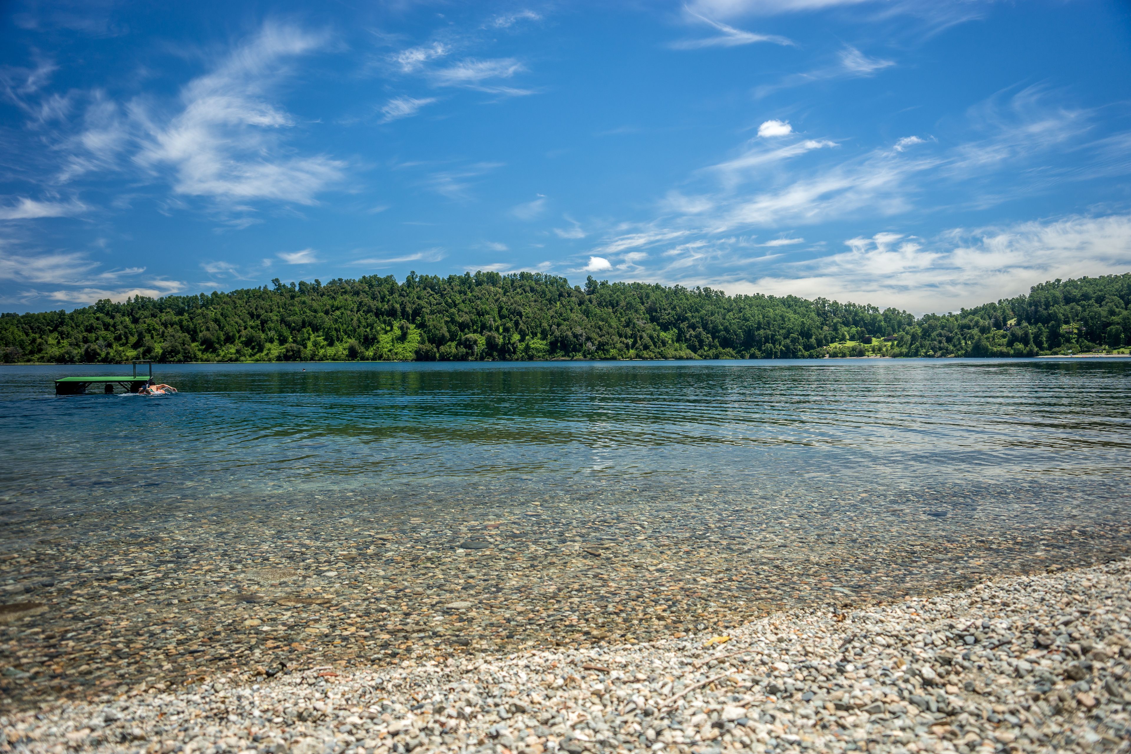 En klar sjö med en stenstrand och en skogbeklädd kulle i bakgrunden.