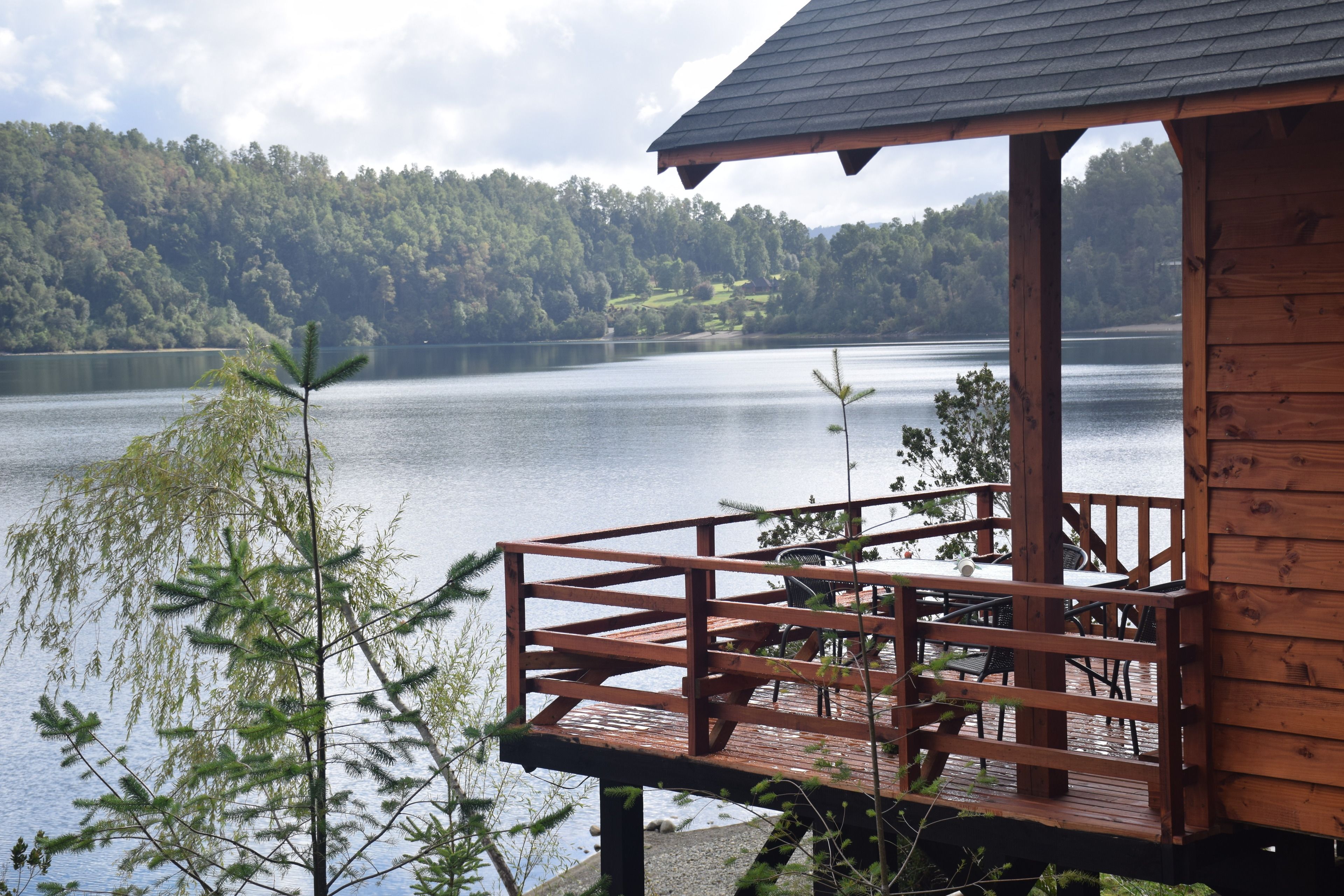 A wooden cabin with a deck overlooking a lake, surrounded by trees.