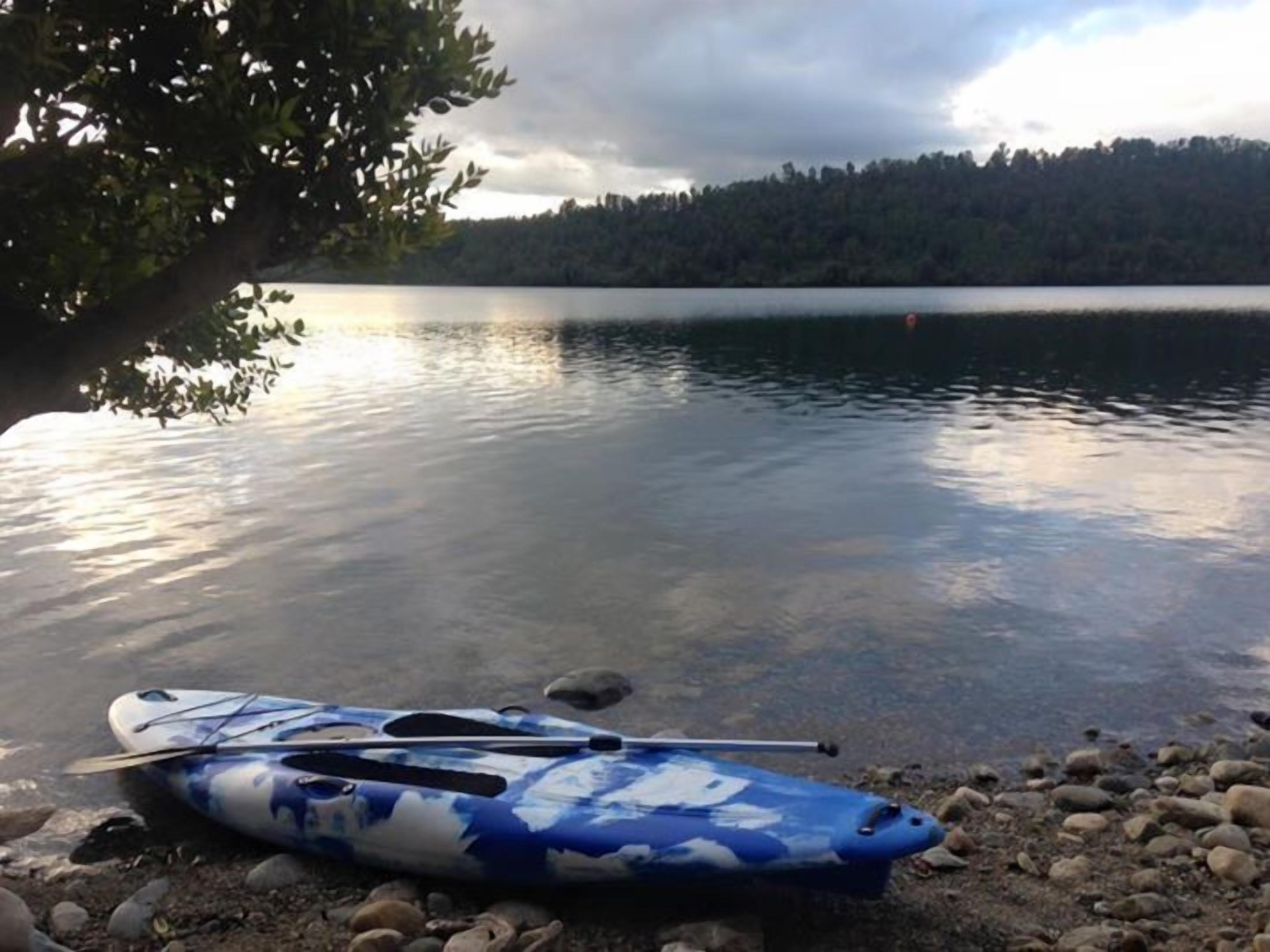 Un kayak su una riva rocciosa, vicino a un lago calmo con una foresta sullo sfondo.