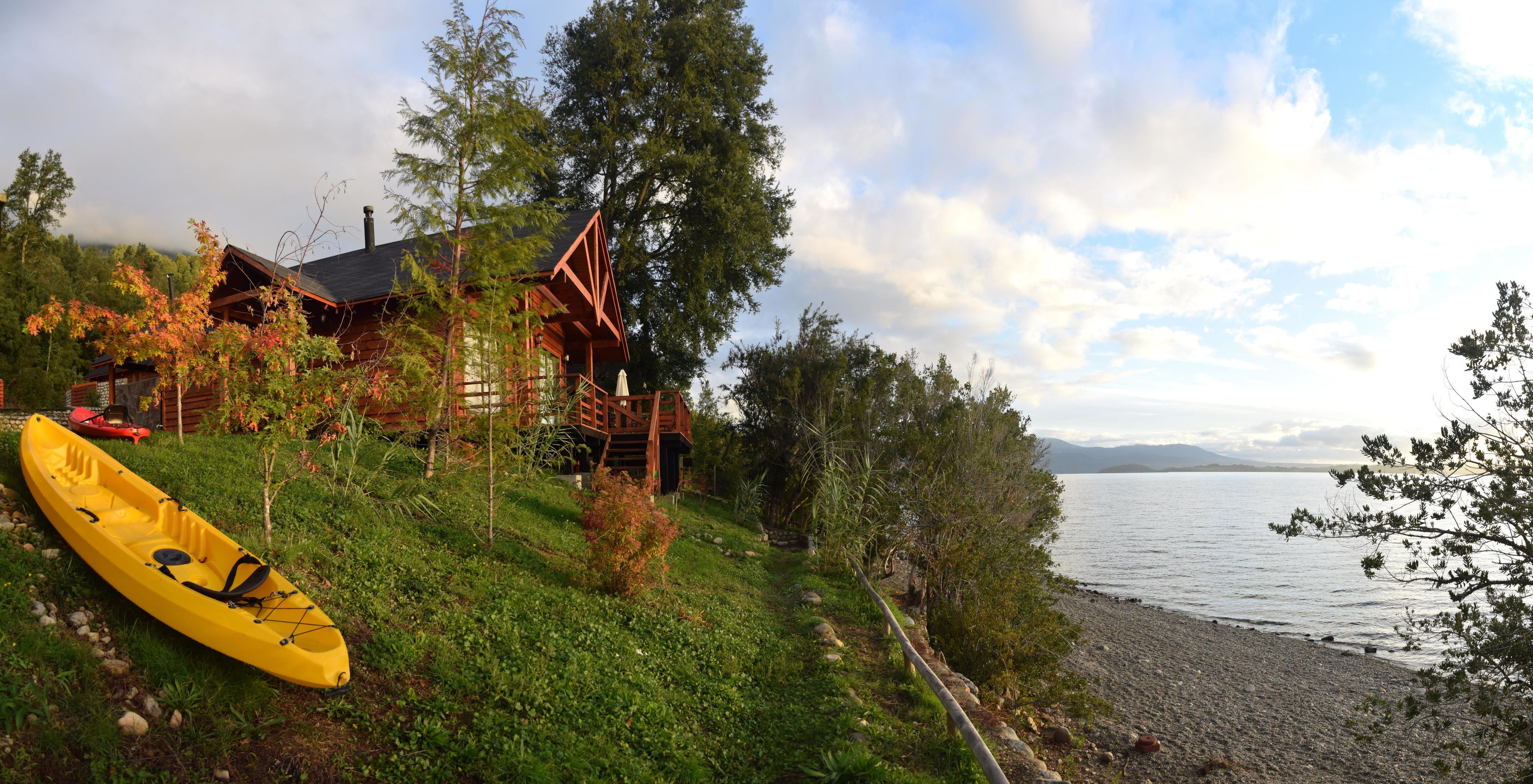 Une cabane avec une terrasse donnant sur un lac, un kayak jaune et un canoë rouge.