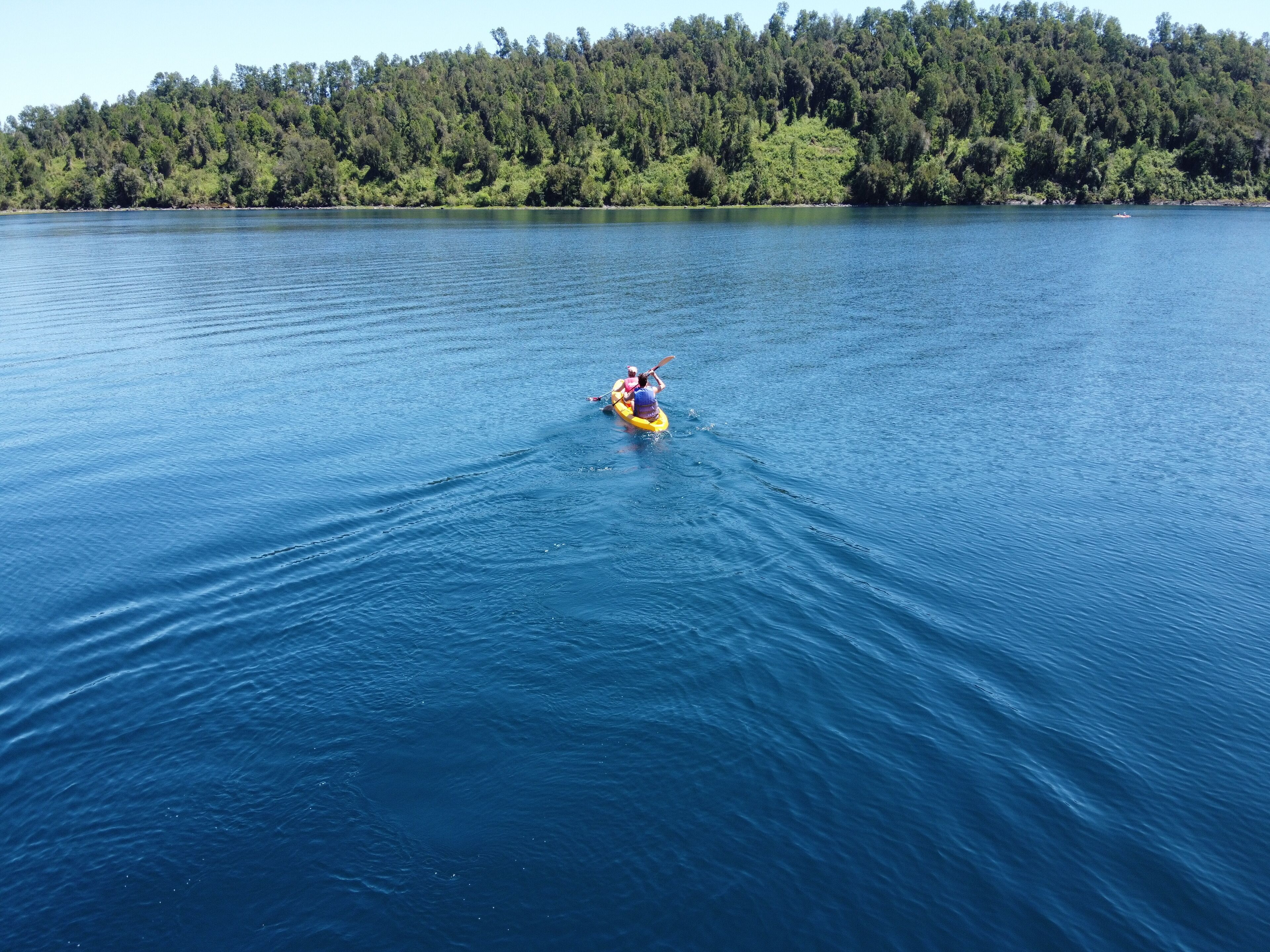 Un kayakiste sur un lac paisible, bordé d’une rive boisée.
