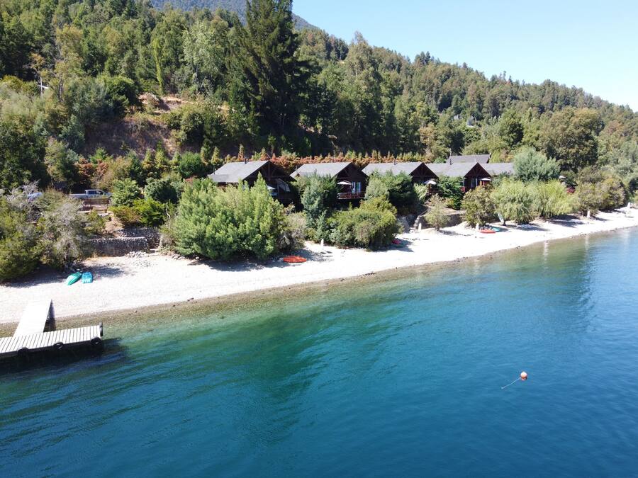 Un complexe hôtelier au bord d’un lac, avec des chalets, un quai et une eau cristalline.