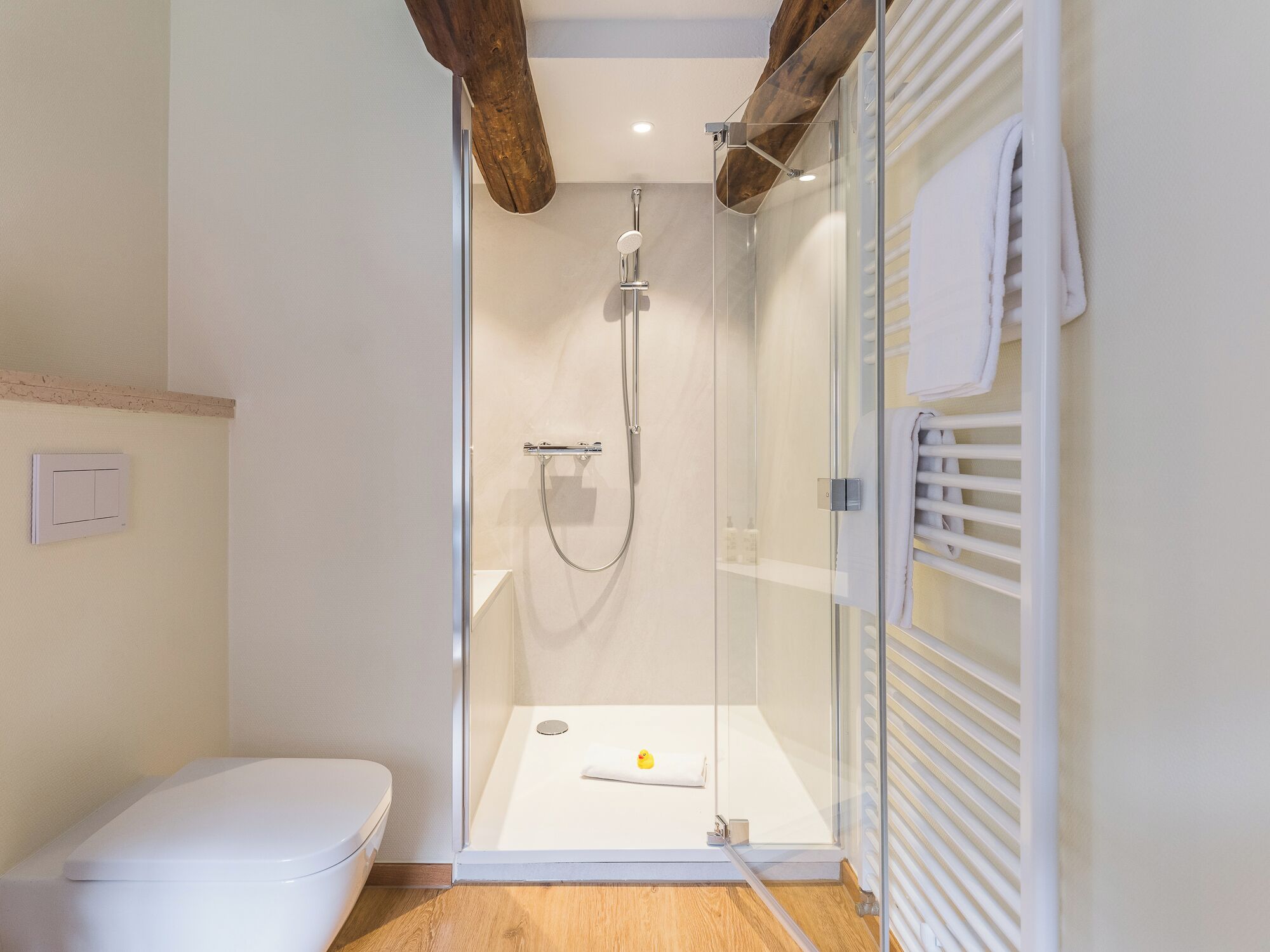 Un baño moderno con ducha de vidrio, inodoro blanco y viga de techo de madera.
