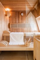 Eine Sauna mit Holzwänden und -bänken, einer Uhr und einem Holzeimer mit Bürste.