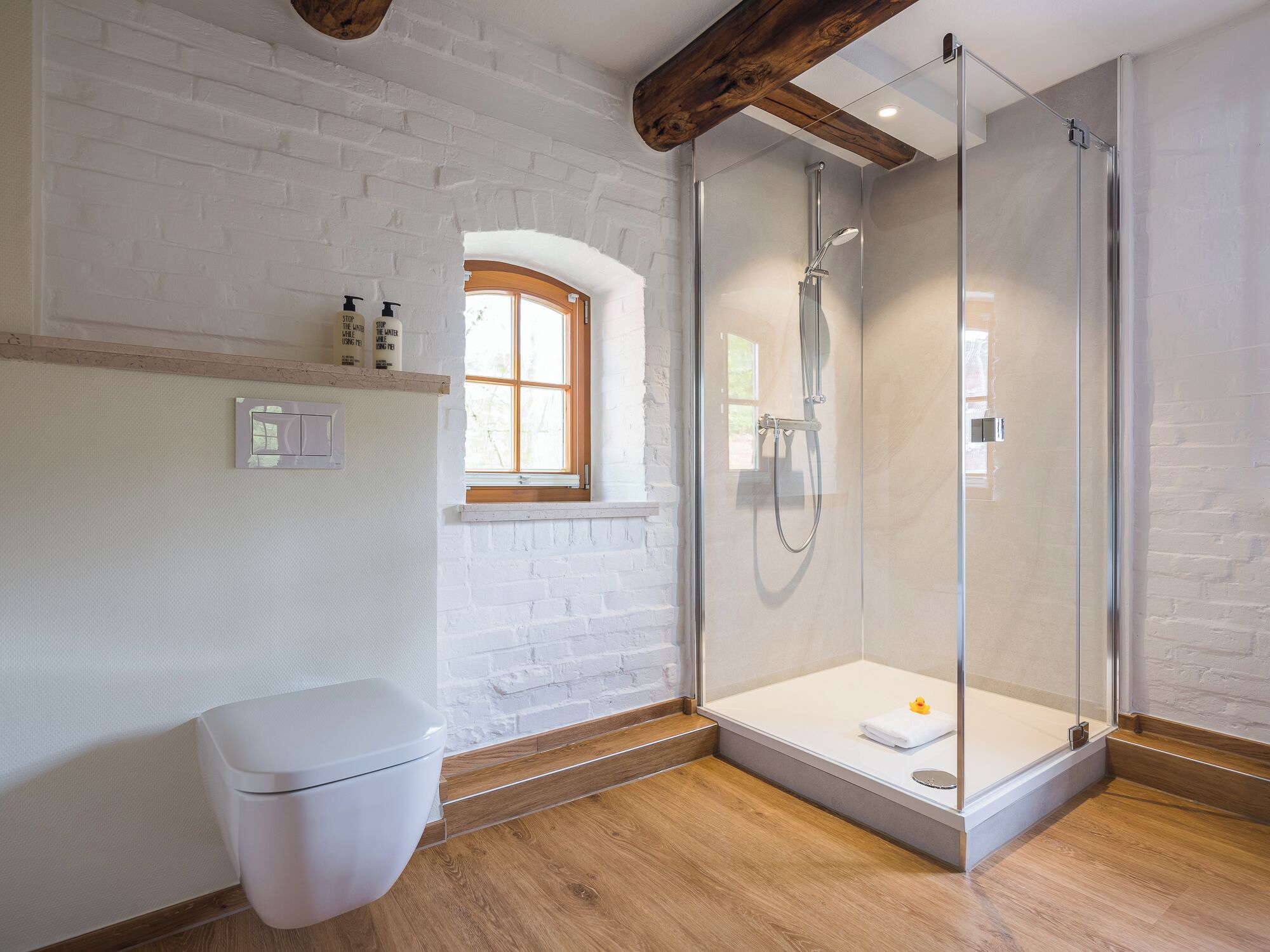 A modern bathroom with a glass-enclosed shower, a white toilet, and a small window.