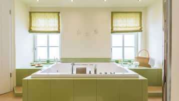 Un baño moderno con una bañera grande, muebles de color verde y dos ventanas con cortinas verdes.
