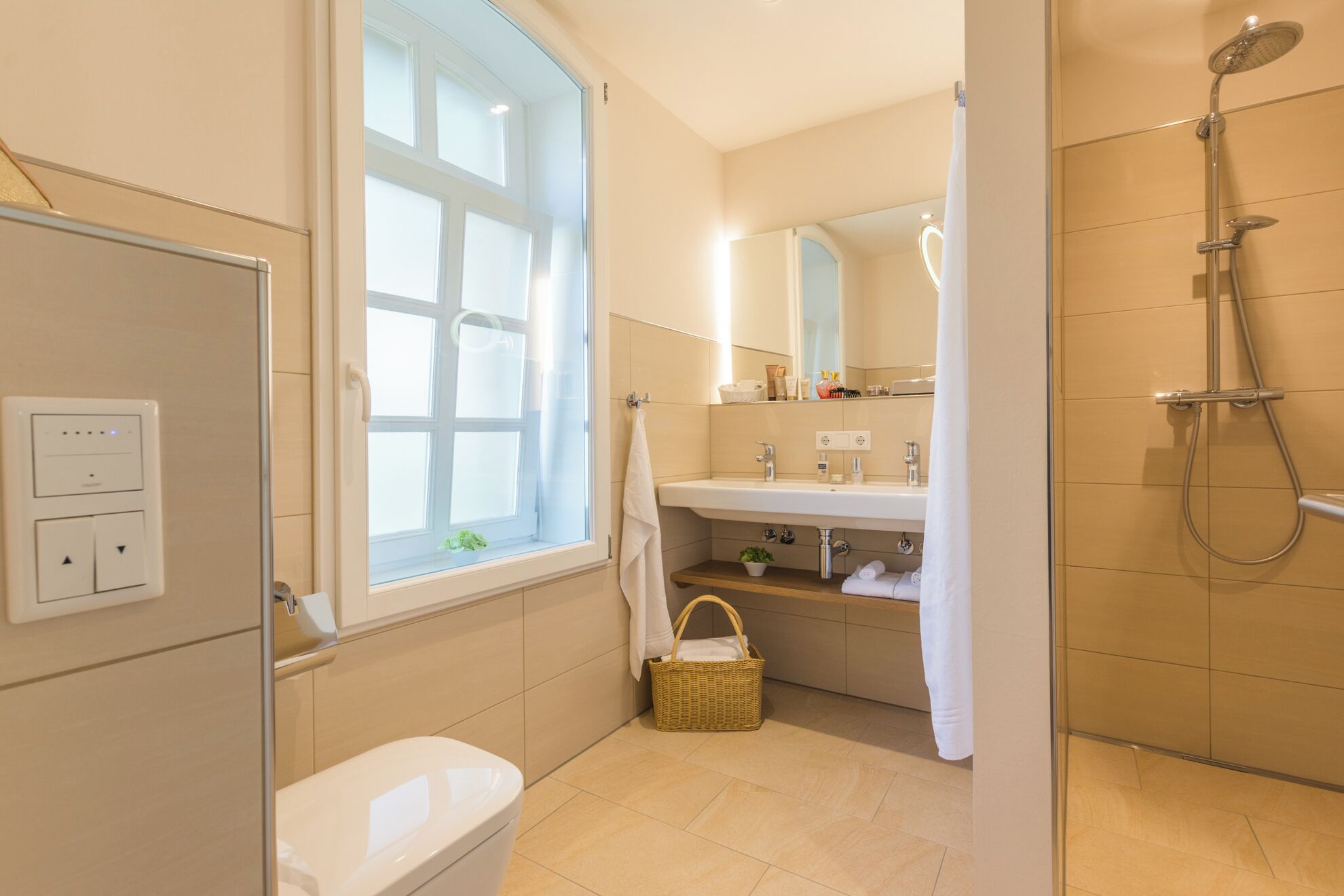 A modern bathroom with a toilet, a shower, a sink, and a window.