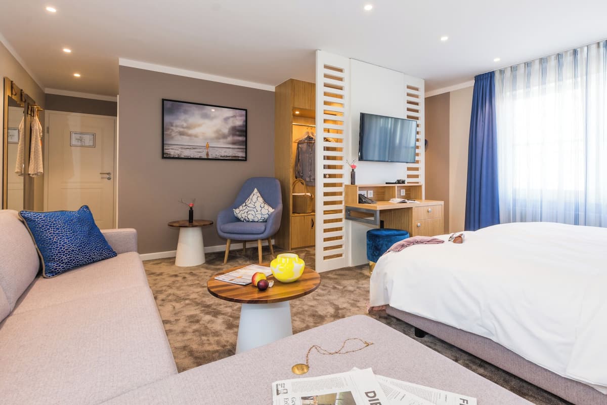 Une chambre d’hôtel avec un lit, un canapé, un bureau, une chaise, une télévision et un tableau au mur.